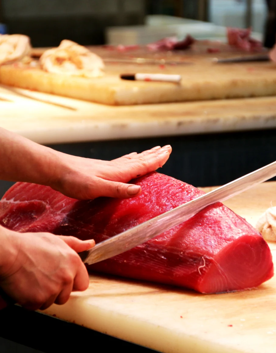 A fishmonger slicing a block of fresh bluefin tuna at a fish market